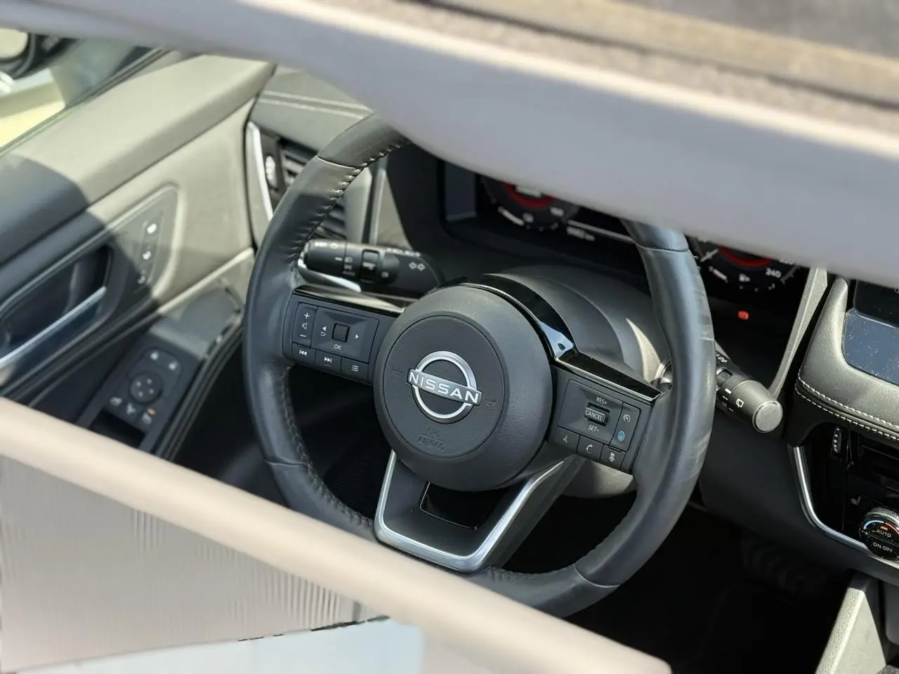 Vue rapprochée du volant cuir noir du Nissan X-TRAIL 2024 avec commandes intégrées et tableau de bord digital.