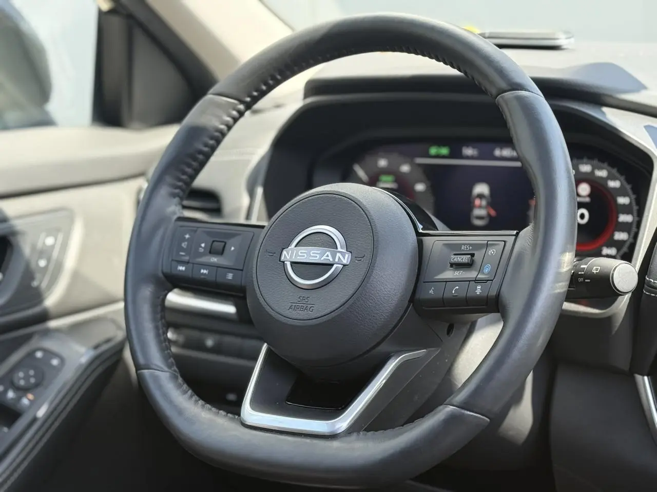 Vue rapprochée du volant en cuir noir du Nissan X-TRAIL 2024 avec commandes intégrées et tableau de bord digital.