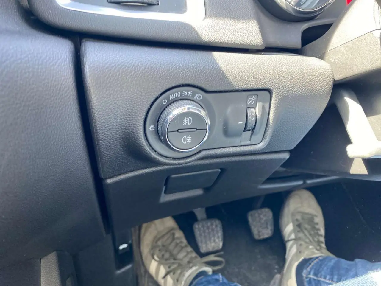 Gros plan sur le tableau de bord côté gauche de l'Opel Astra Sports Tourer gris, avec commandes des phares et pédales manuelles visibles.