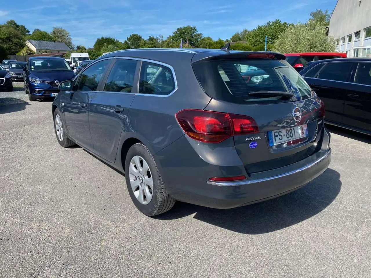Opel Astra Sports Tourer gris vue 3/4 arrière droit, avec feux arrière rouges et toit avec antenne shark fin.
