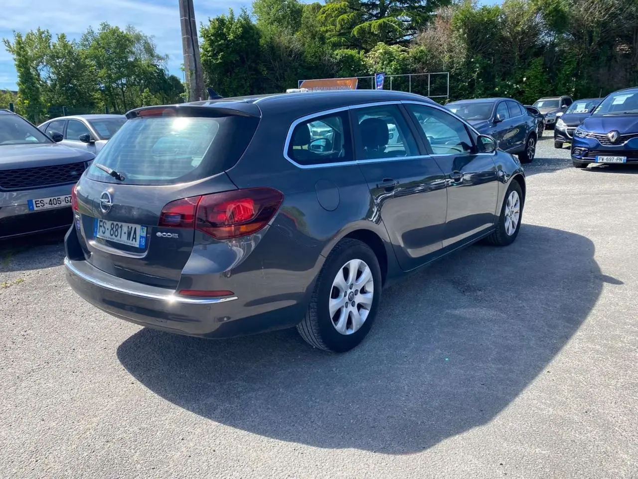 Opel Astra Sports Tourer gris vue 3/4 arrière droit, avec feux arrière rouges et jantes blanches.