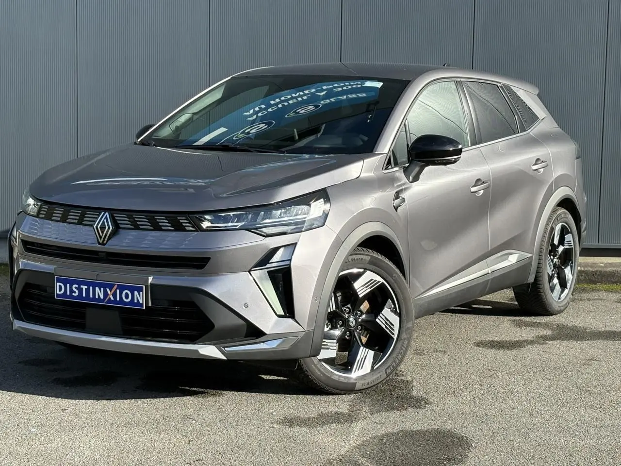 Renault Symbioz E-Tech gris Cassiopée en 3/4 avant droit, avec jantes 18 pouces et calandre distinctive.
