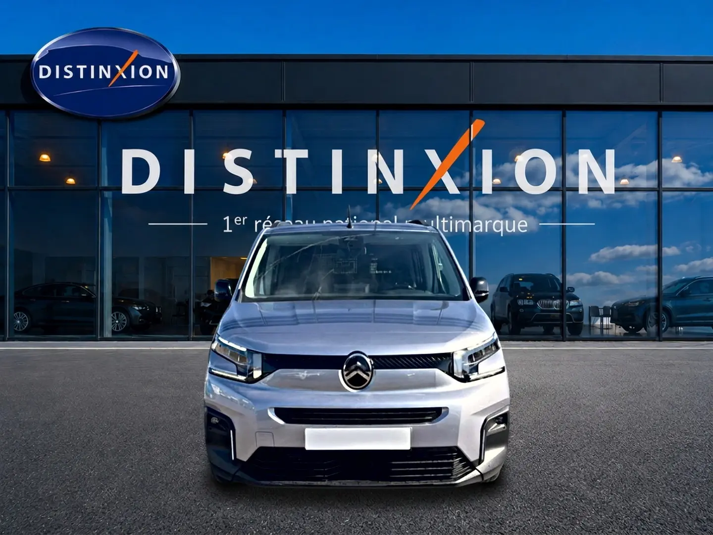 Vue avant d'un Citroën Berlingo 2026 gris acier, avec calandre noire et phares LED devant un bâtiment vitré.