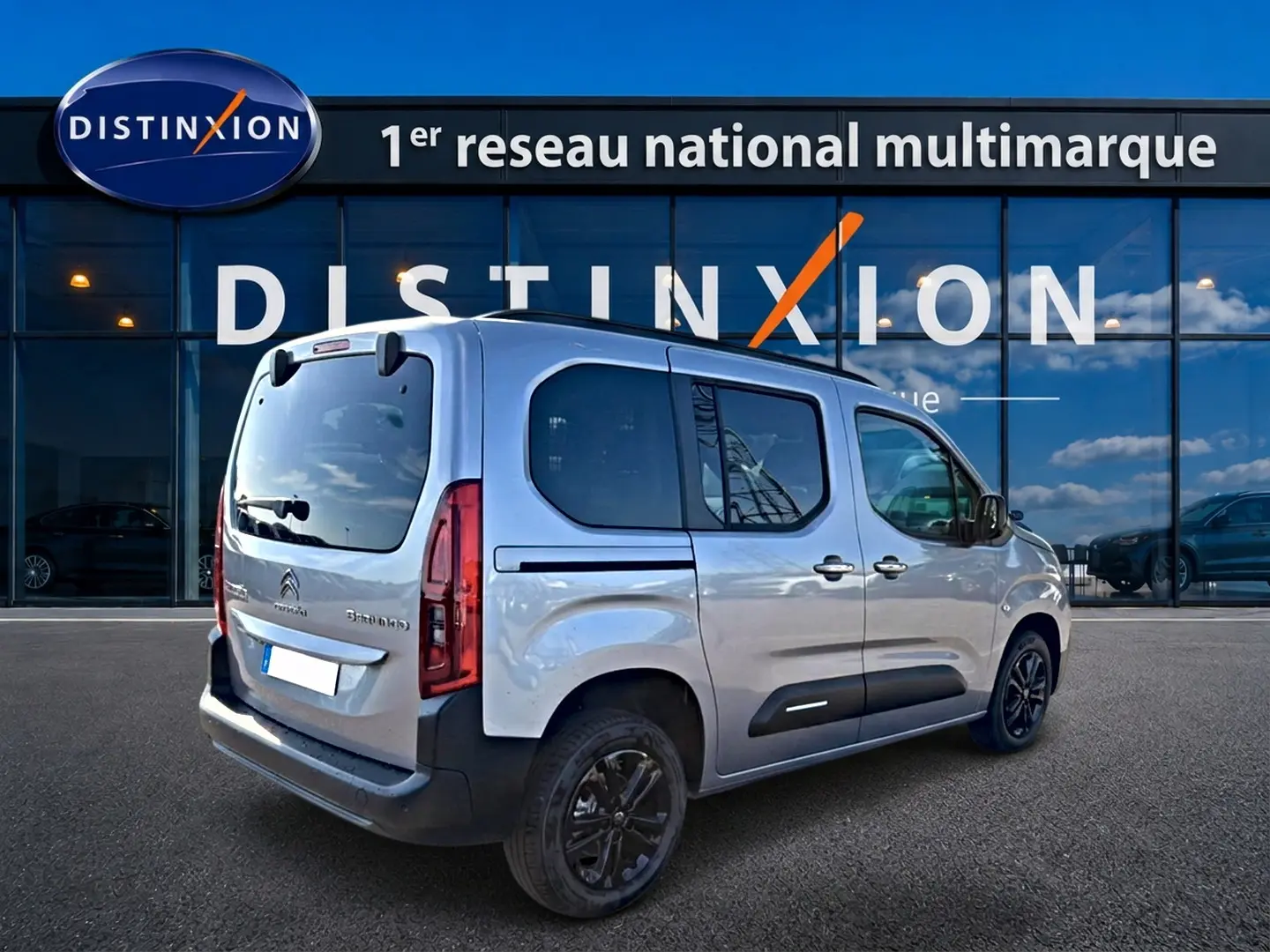 Vue 3/4 arrière droite d'un Citroën Berlingo Steel Grey 2026 avec barres de toit et jantes alu noires.