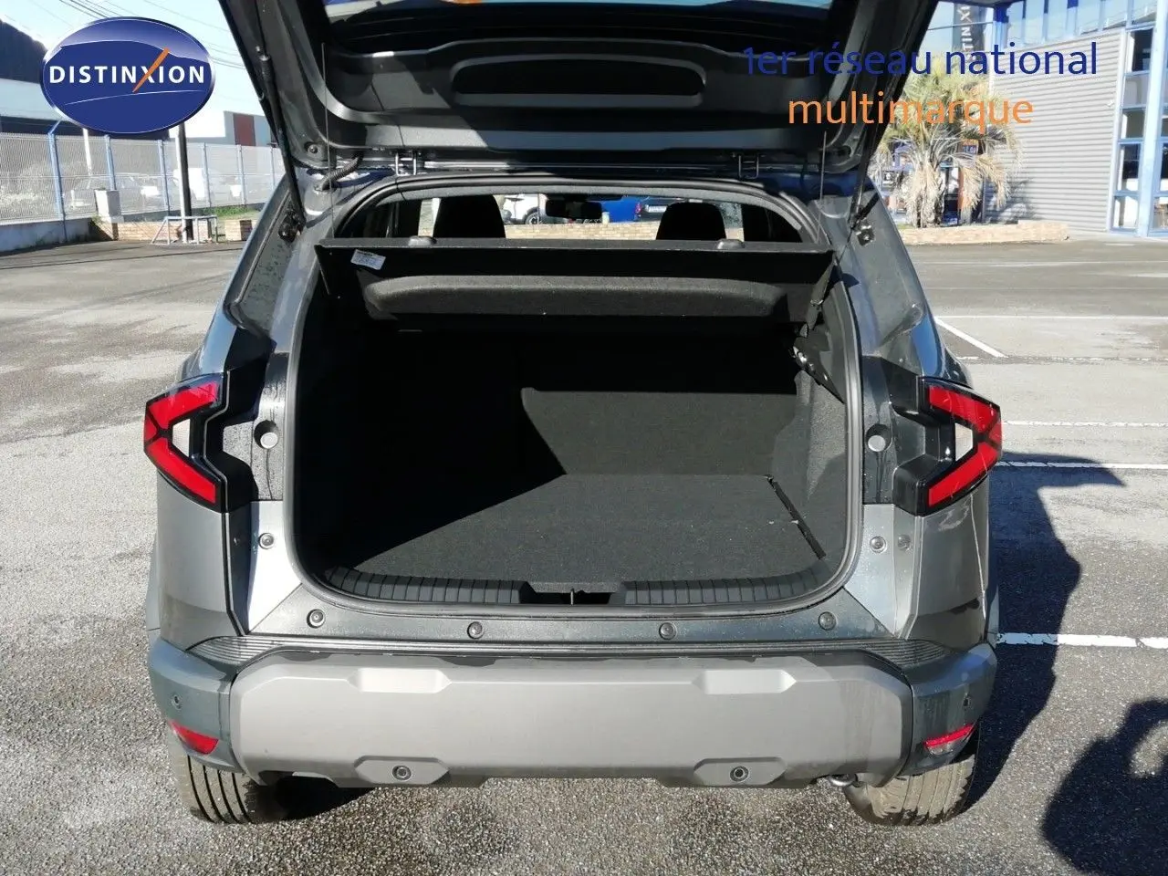 Vue arrière du Dacia Duster TCE MHEV 140ch Journey gris schiste métal avec coffre ouvert et feux arrière allumés.