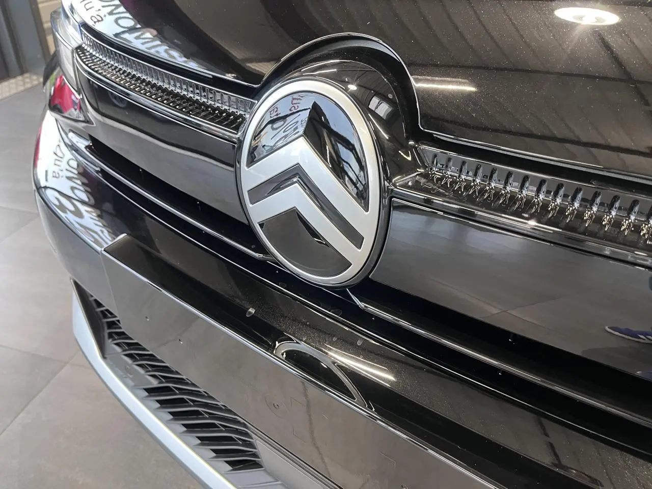 Gros plan sur la calandre avant noire métallisée d'une Citroën C4 2025 avec logo chrome distinctif au centre.