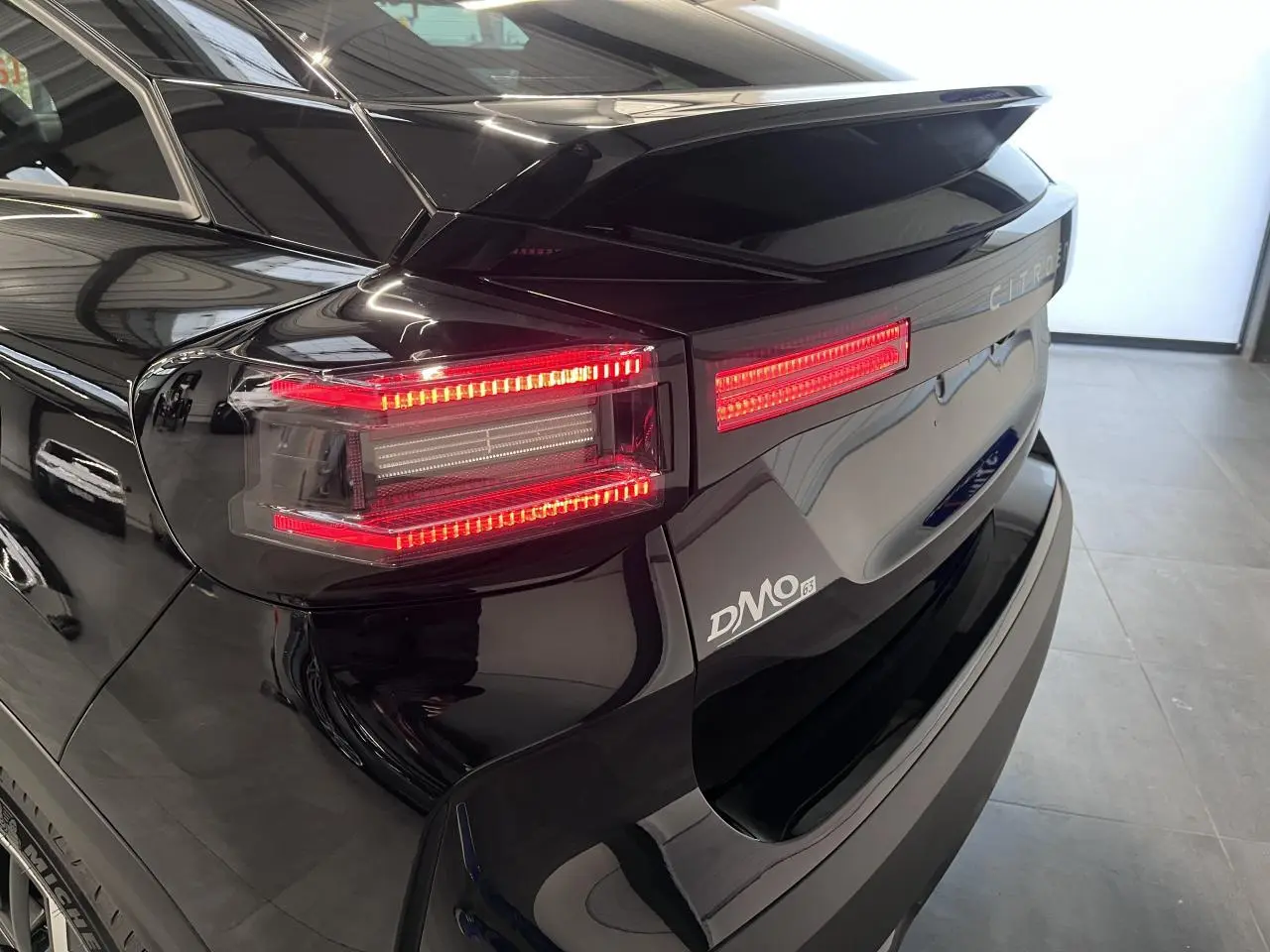 Feu arrière droit allumé et hayon noir métallisé d'une Citroën C4 hybride 2025 vue en 3/4 arrière.