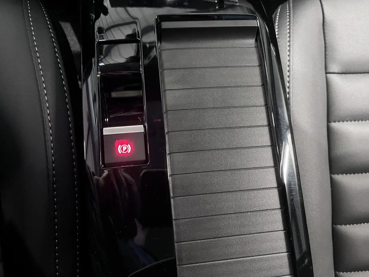 Gros plan sur la console centrale noire brillante de la Citroën C4 2025 avec bouton de frein de stationnement électrique allumé.