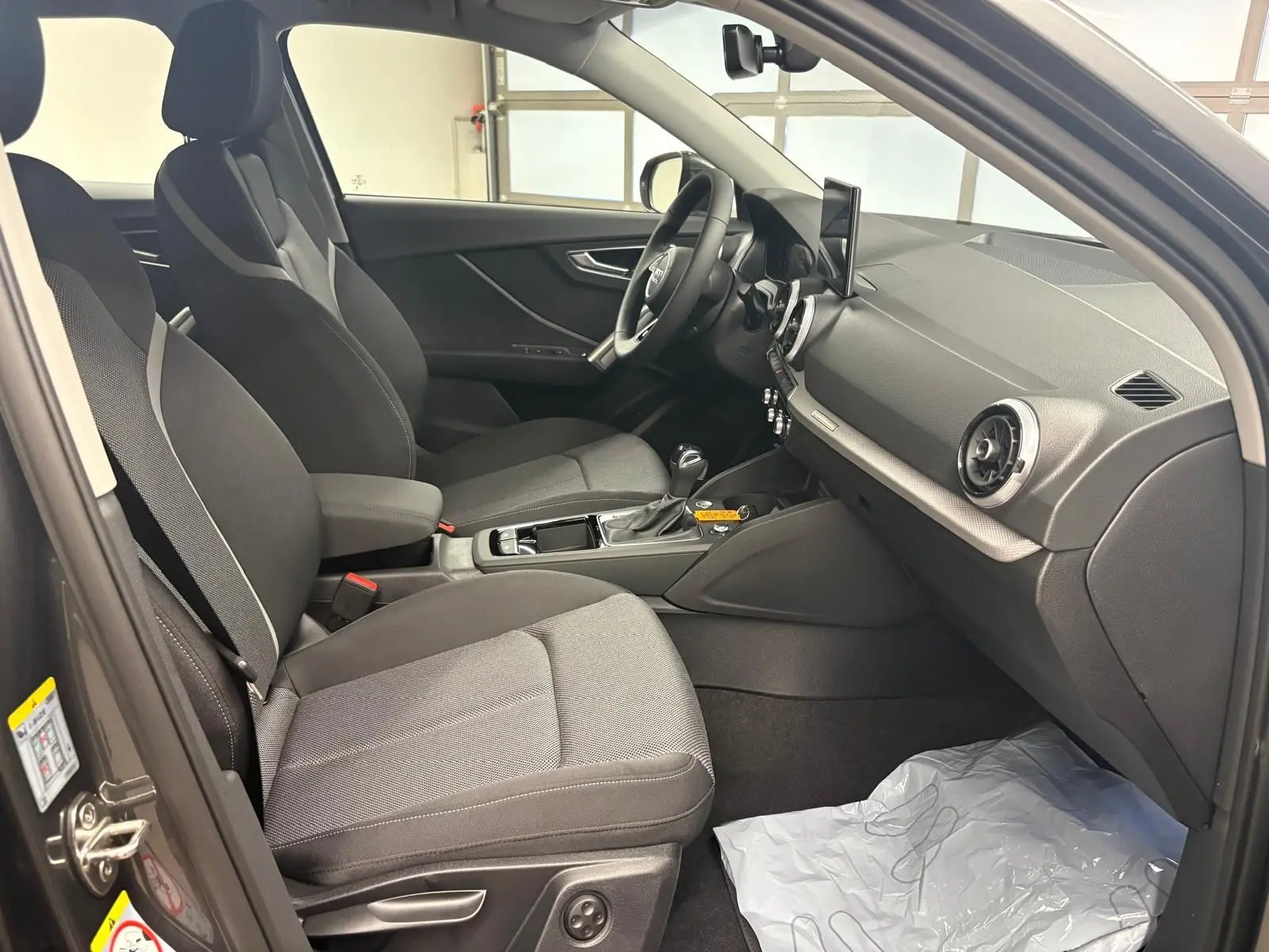 Intérieur avant droit de l’Audi Q2 35 TFSI 150 S tronic 7 S line avec sièges tissu gris et tableau de bord noir.