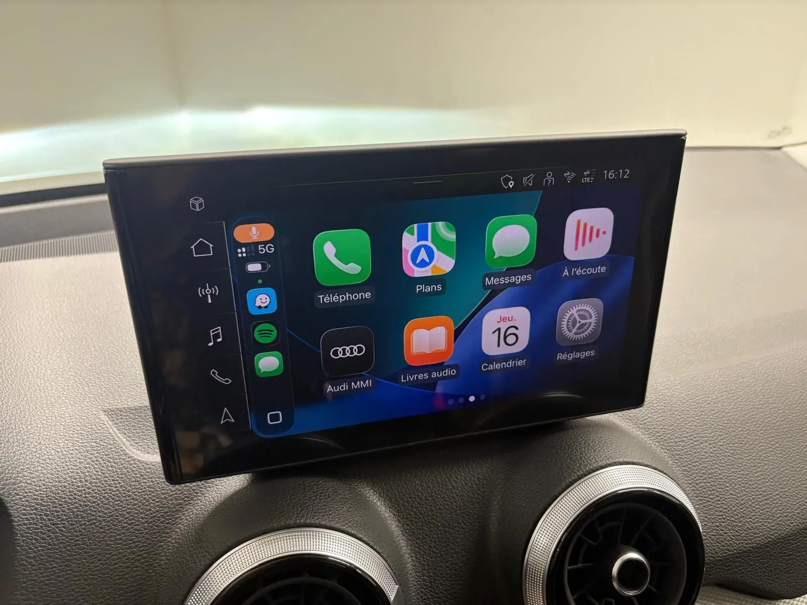 Écran tactile central de l’Audi Q2 35 TFSI S Line 2026 affichant l’interface Apple CarPlay, avec aérateurs ronds en dessous.