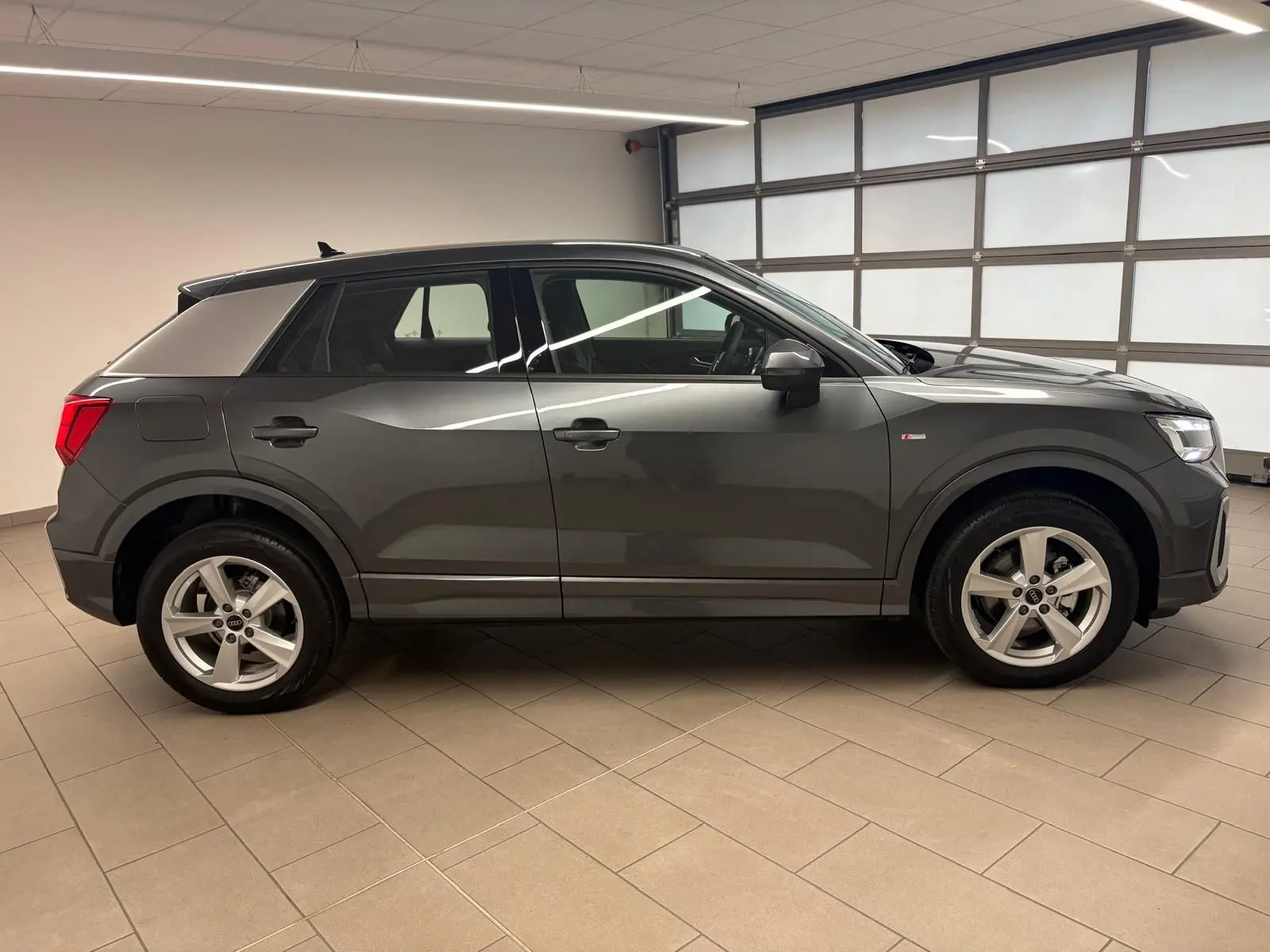 Audi Q2 35 TFSI S Line gris Daytona vue de profil côté gauche en intérieur, avec jantes alliage et toit noir.