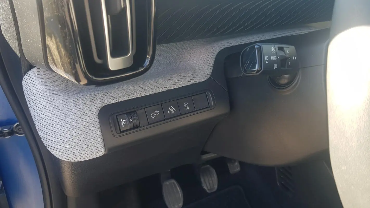 Détail intérieur côté gauche du tableau de bord bleu foncé de la Citroën C3 2024 avec commandes d’éclairage et pédales visibles.