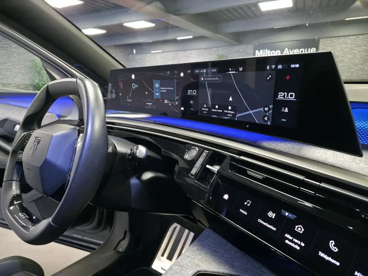 Vue intérieure du tableau de bord et volant cuir noir laqué du Peugeot 3008 gris avec écran panoramique 21 pouces affichant la navigation.