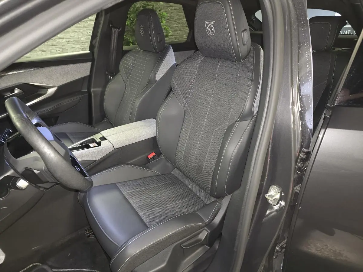 Vue intérieure côté conducteur du Peugeot 3008 gris 2025, sièges tissu et cuir avec logo Peugeot brodé sur les appuie-têtes.