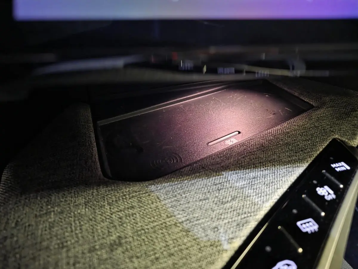 Détail du chargeur sans fil intégré dans la console centrale tissu gris du Peugeot 3008 hybride 2025.