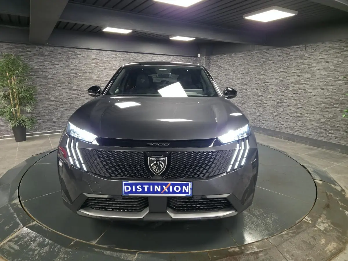 Vue frontale d'un Peugeot 3008 gris métallisé 2025 avec calandre noire et feux LED à griffes distinctifs allumés.