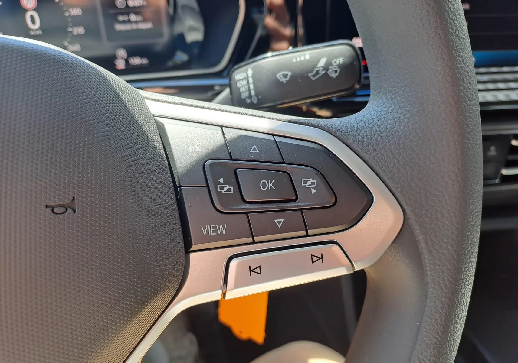 Gros plan sur les commandes au volant côté gauche du Volkswagen Caddy Cargo Maxi blanc, avec boutons multifonctions et tableau de bord partiel.