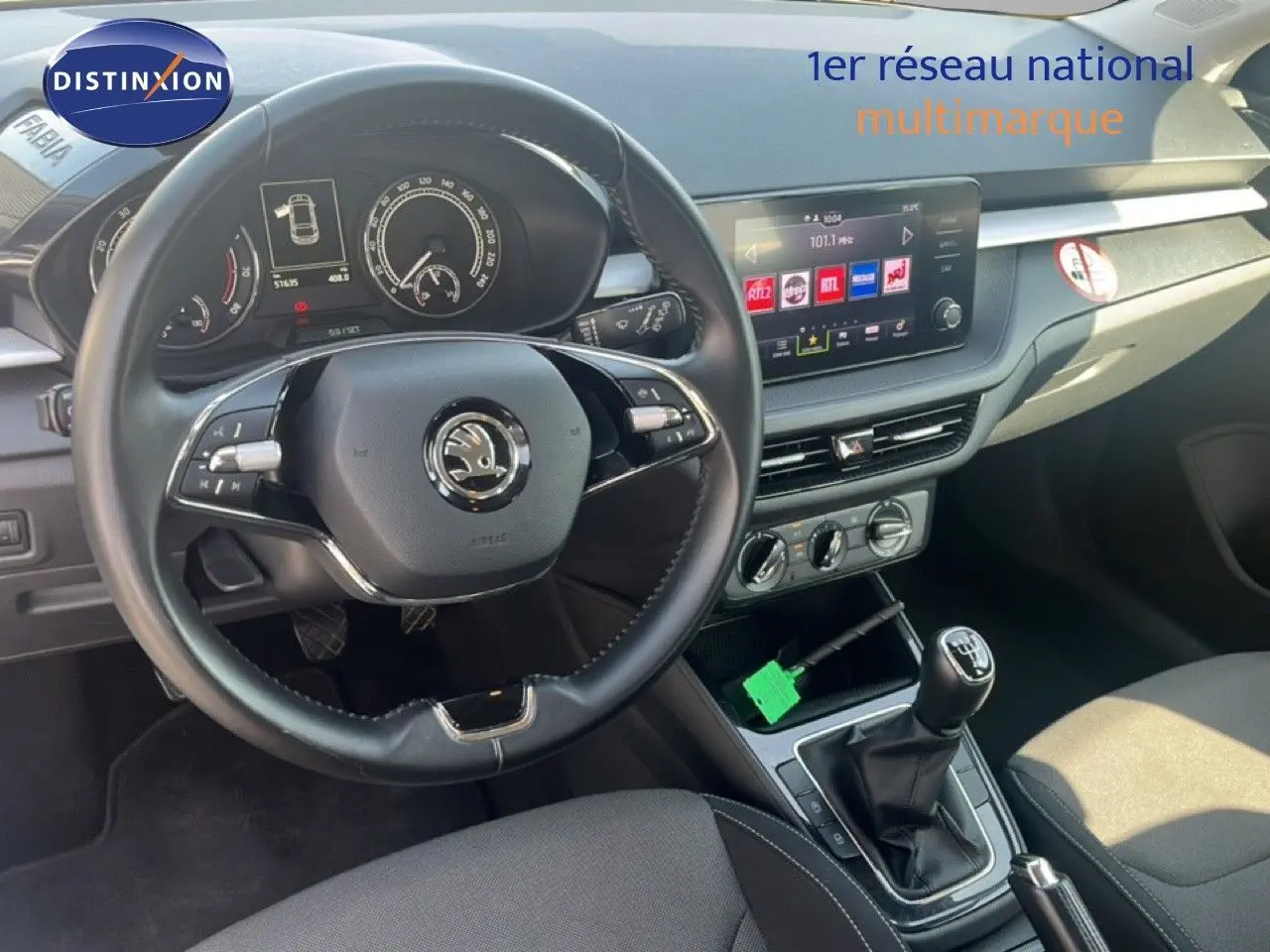 Vue intérieure de face du poste de conduite d'une Skoda Fabia blanche, avec volant cuir multifonction et écran tactile central.