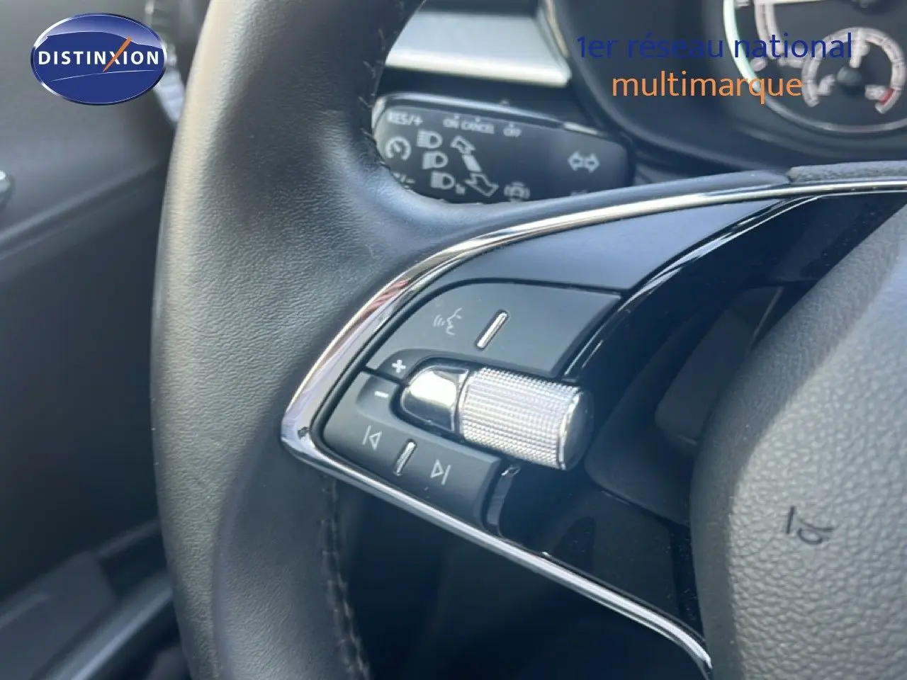 Gros plan sur les commandes multifonctions en chrome et noir du volant d'une Skoda Fabia blanche, intérieur noir.