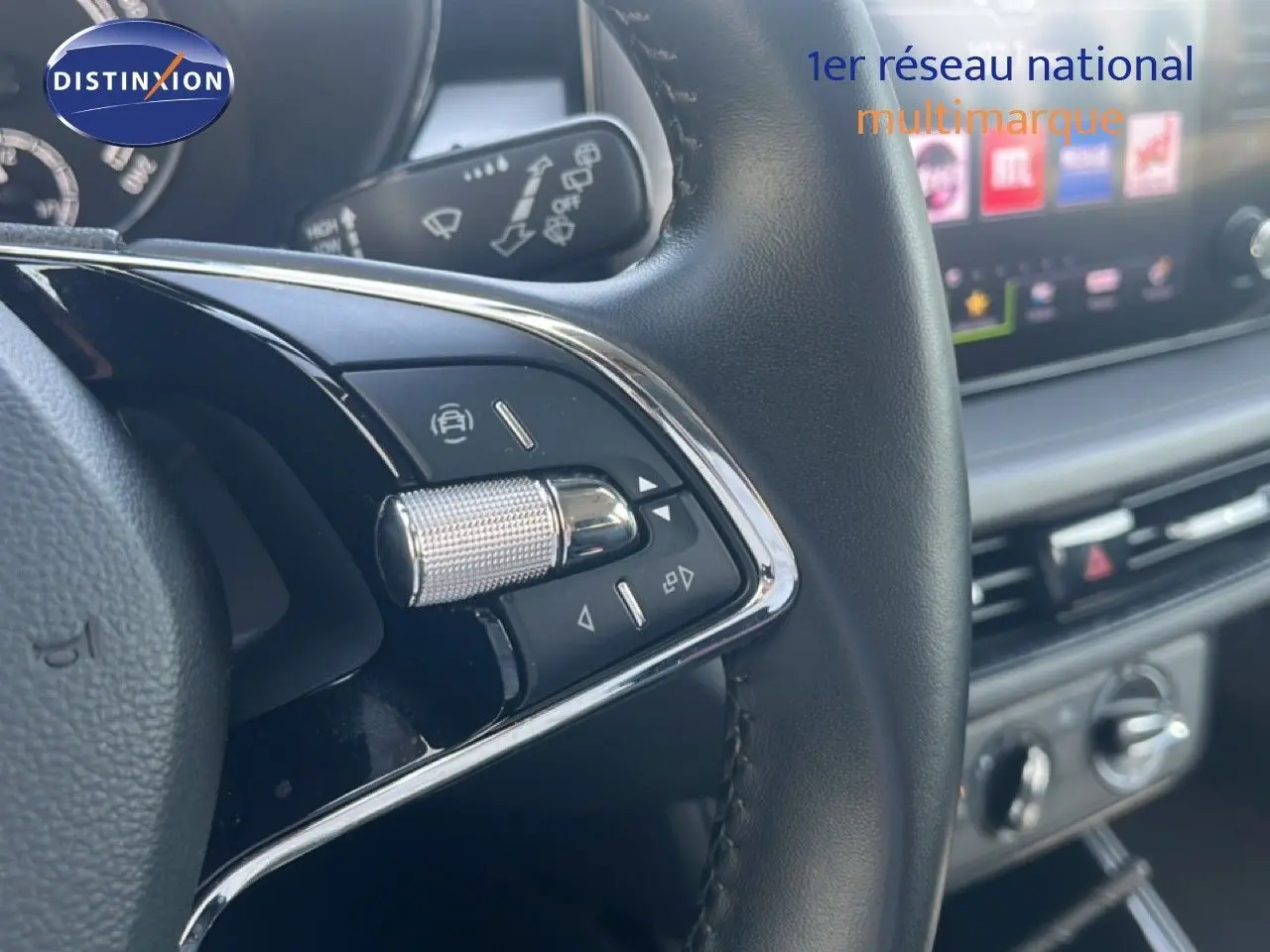 Gros plan sur la commande multifonction du volant noir d’une Skoda Fabia blanche, avec tableau de bord et écran tactile en arrière-plan.