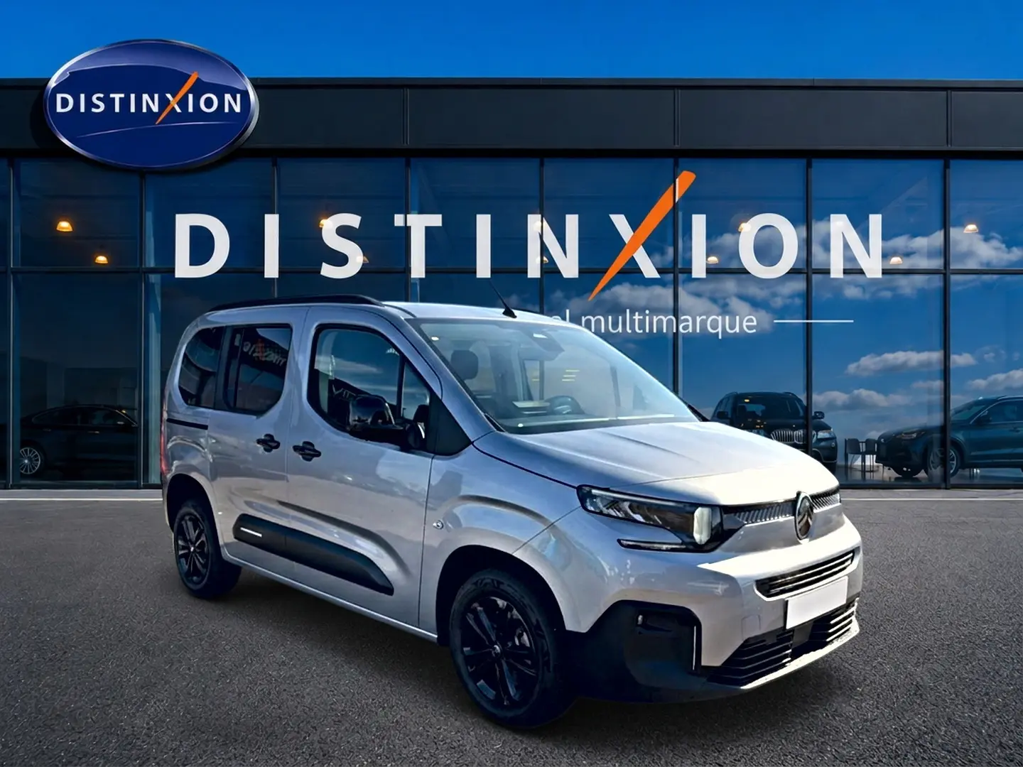 Vue 3/4 avant droite du Citroën Berlingo Steel Grey avec barres de toit et jantes noires devant showroom Distinxion.
