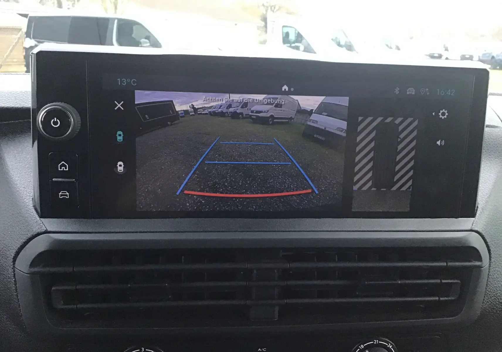 Écran central affichant la caméra de recul avec vue arrière sur un parking de fourgons blancs.