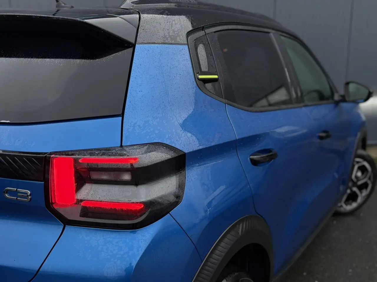 Vue 3/4 arrière droite d'une Citroën C3 2025 Bright Blue avec toit noir Perla et feux arrière LED 3D allumés.
