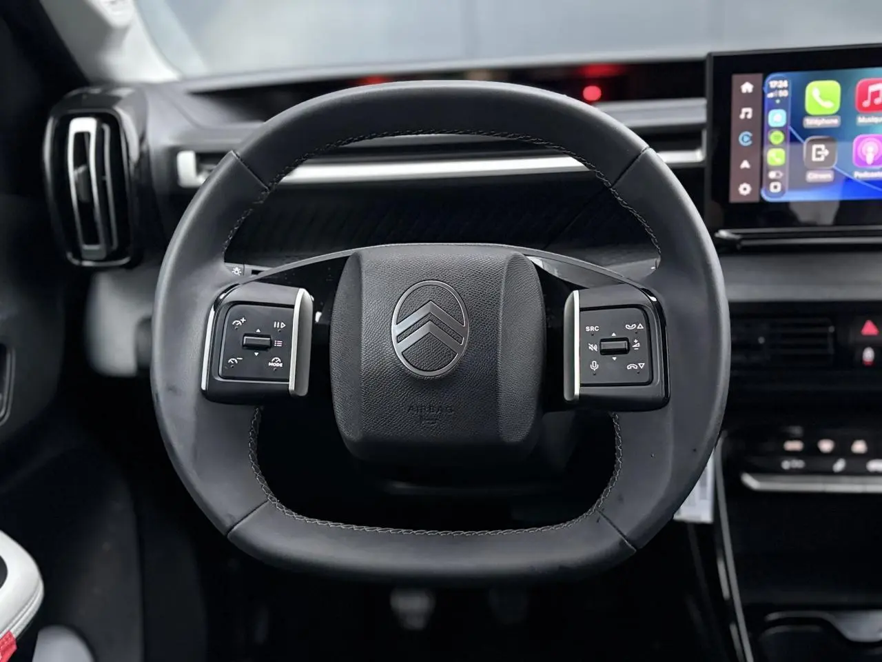 Vue rapprochée du volant noir de la Citroën C3 2025 avec commandes intégrées et écran tactile en arrière-plan.