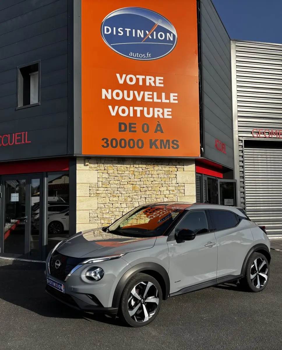 Nissan Juke Hybrid gris clair vue 3/4 avant droit, avec toit noir et jantes alliage distinctives.