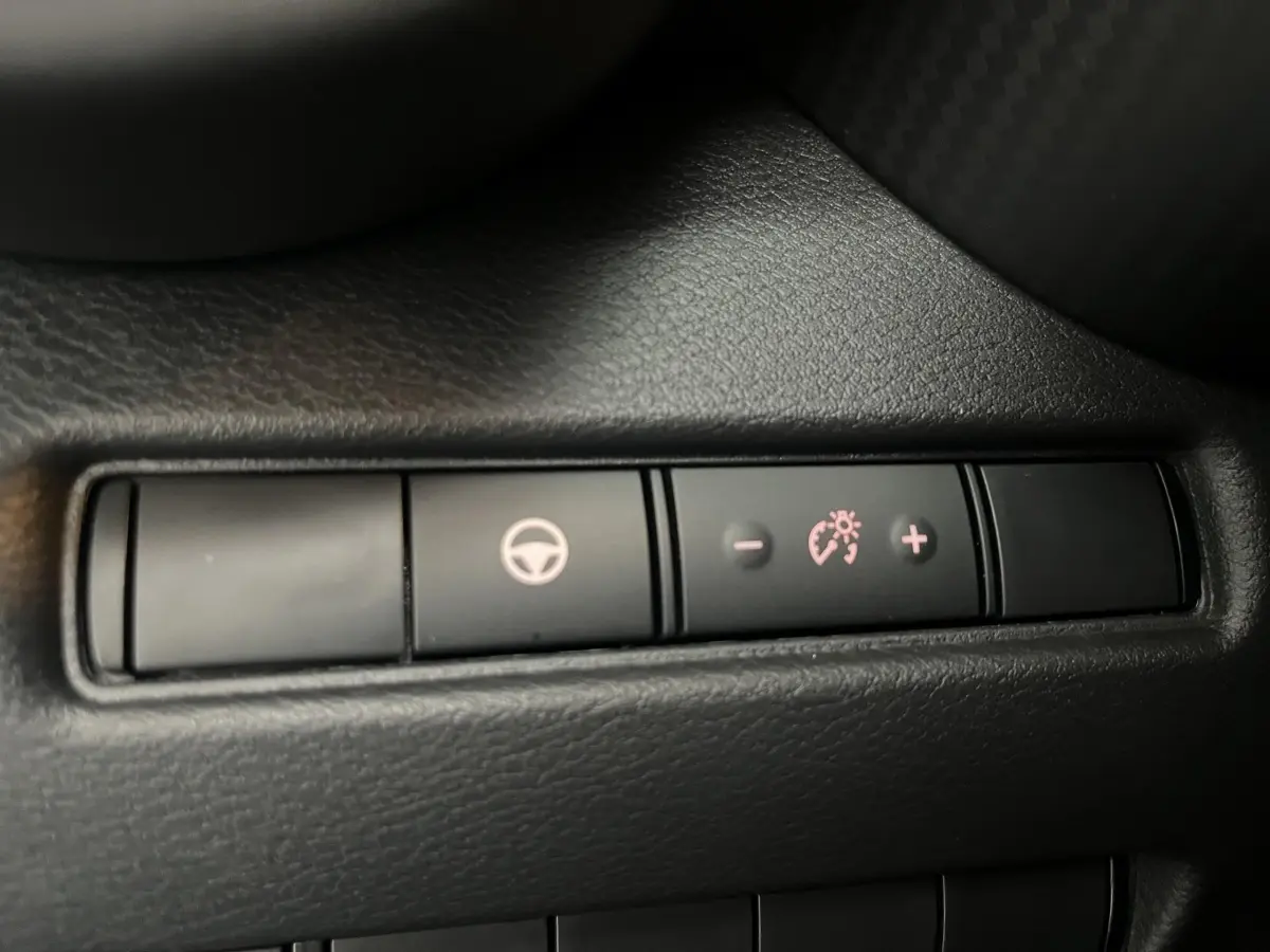 Gros plan sur les boutons de réglage du régulateur de vitesse sur la console intérieure noire du Nissan Juke Hybrid 2024.