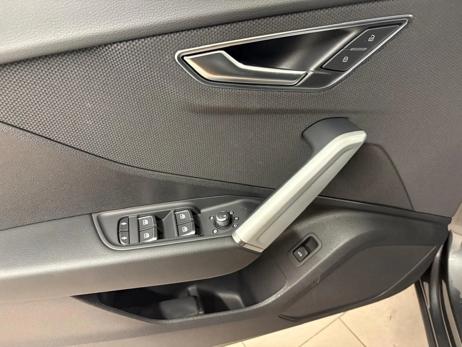 Gros plan sur la porte côté conducteur de l'Audi Q2 35 TFSI S Line 2026 en Gris Daytona, montrant les commandes de vitres et la poignée argentée.