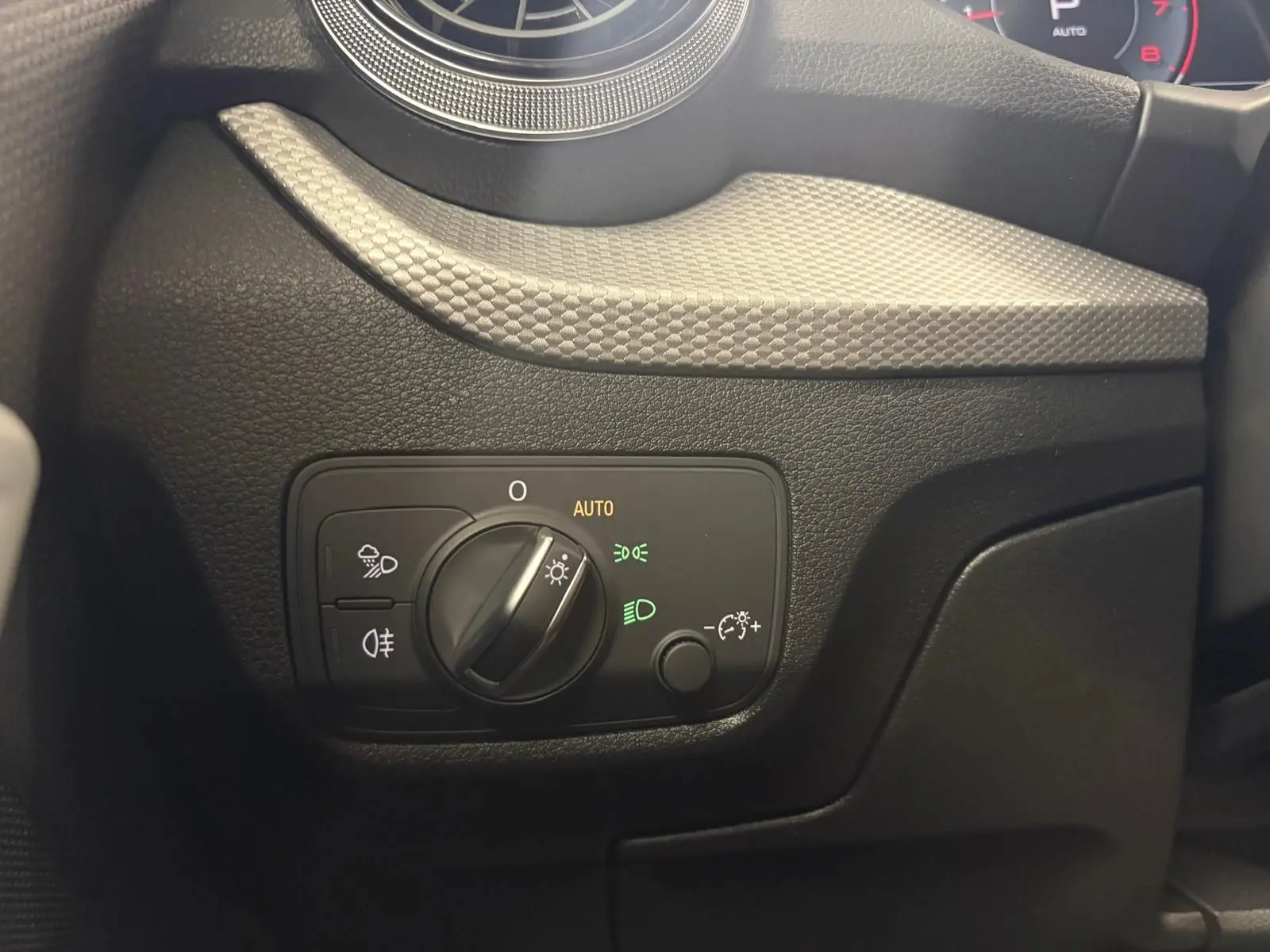 Gros plan sur le bouton de commande des phares à gauche du tableau de bord de l'Audi Q2 35 TFSI S Line 2026.