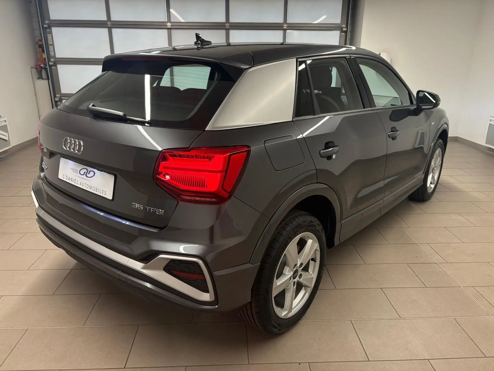 Audi Q2 35 TFSI S Line gris Daytona vue 3/4 arrière droit en intérieur, feux arrière allumés.