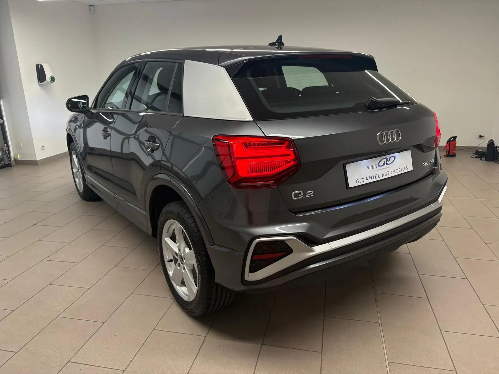 Audi Q2 35 TFSI S Line gris Daytona en 3/4 arrière droit, avec toit noir et montant arrière argenté contrastant.