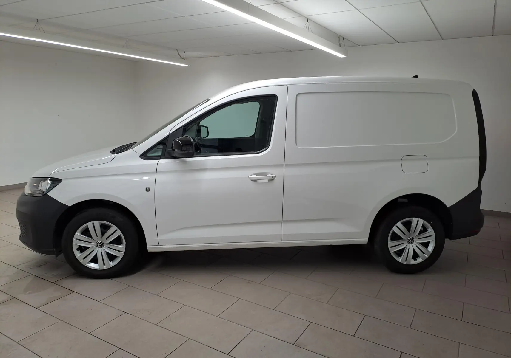 Vue de profil côté gauche d'un Volkswagen Caddy blanc Candy avec rétroviseurs noirs et jantes acier 16 pouces.