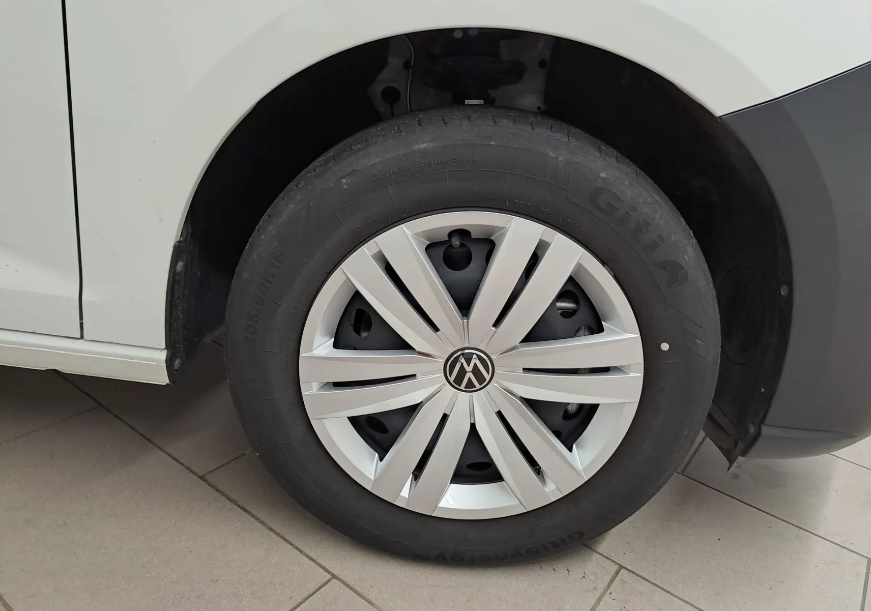 Gros plan sur la roue avant gauche blanche du Volkswagen Caddy 2.0 TDI avec enjoliveur argenté et logo VW central.