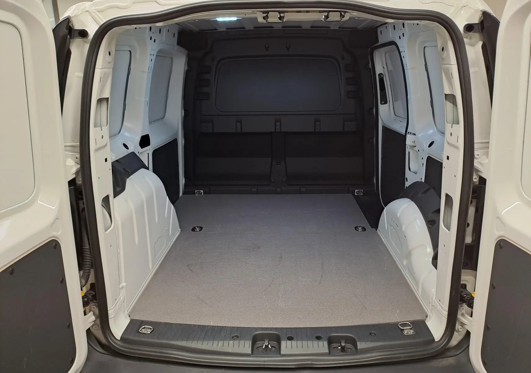 Vue intérieure arrière du coffre blanc du Volkswagen Caddy 2.0 TDI 122 DSG7 Business avec plancher plat et parois métalliques.