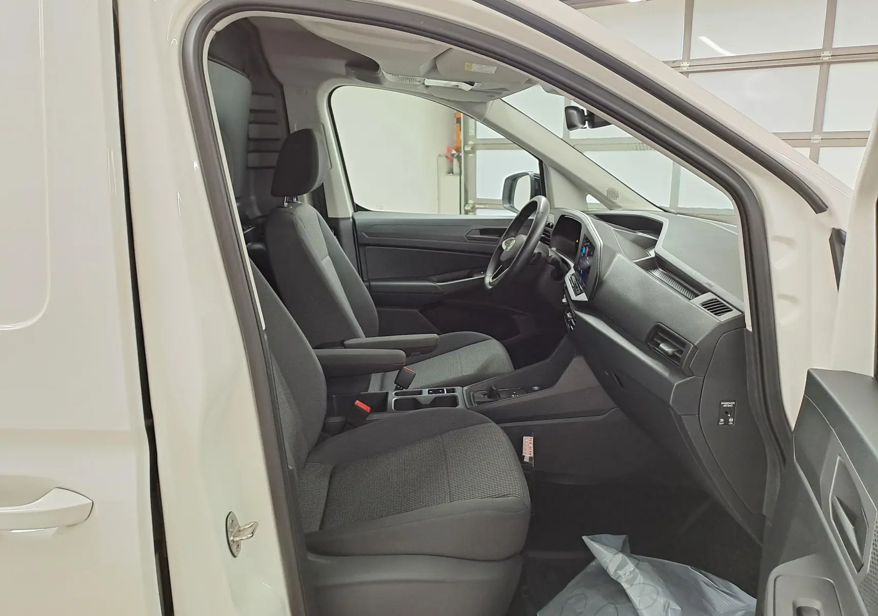 Vue intérieure côté conducteur du Volkswagen Caddy blanc Candy 2025, montrant sièges et tableau de bord moderne.