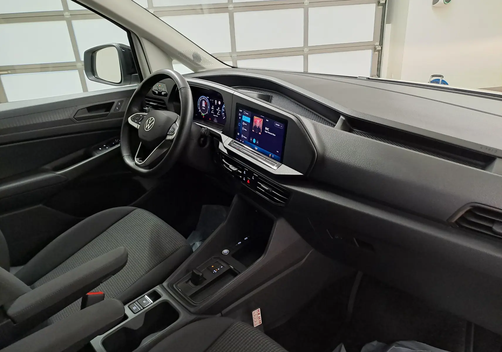 Vue intérieure côté conducteur du Volkswagen Caddy 2025 avec tableau de bord noir et écran tactile central.