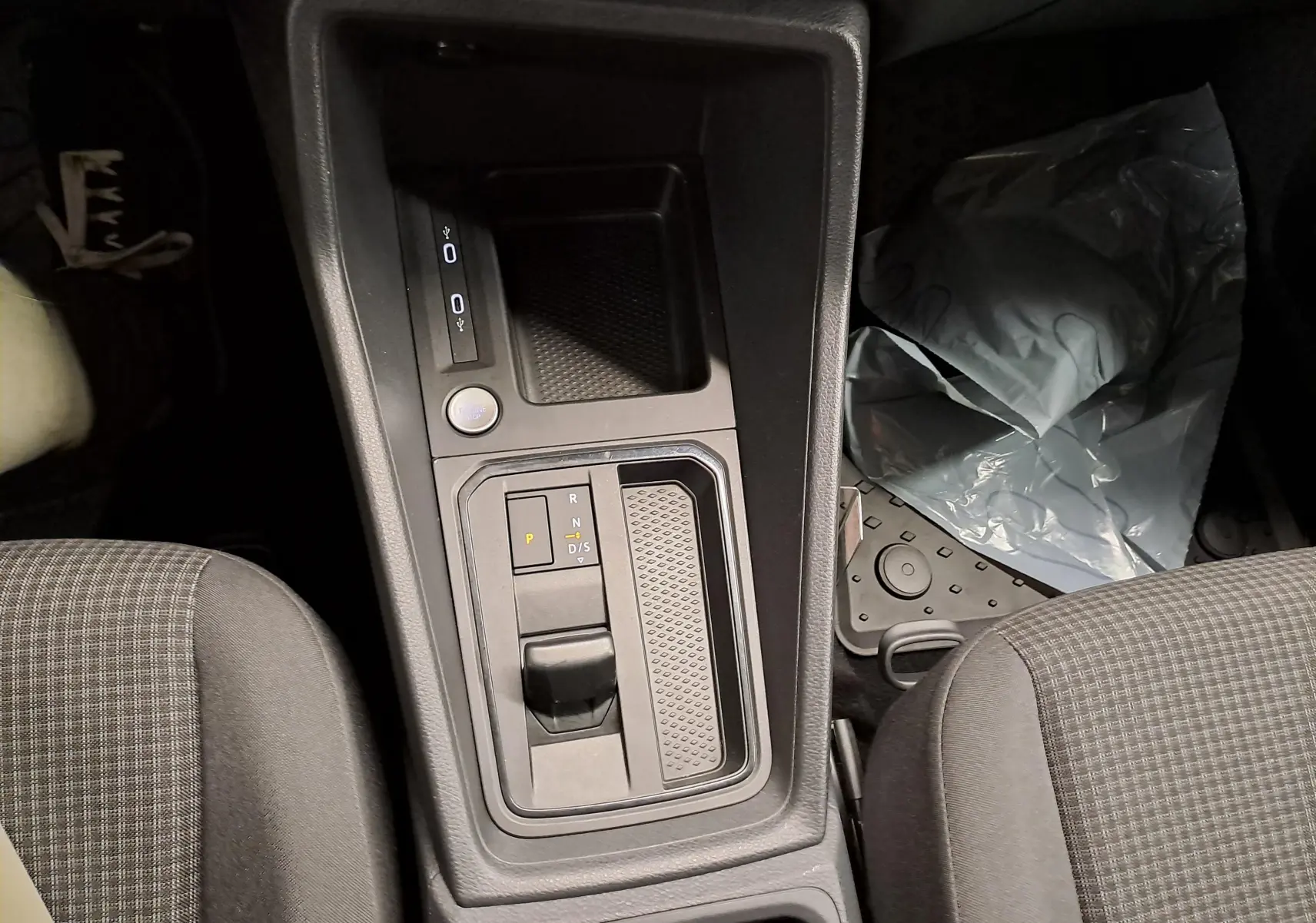 Vue intérieure centrée sur la console centrale avec levier de vitesses automatique et bouton start/stop du Volkswagen Caddy 2025.