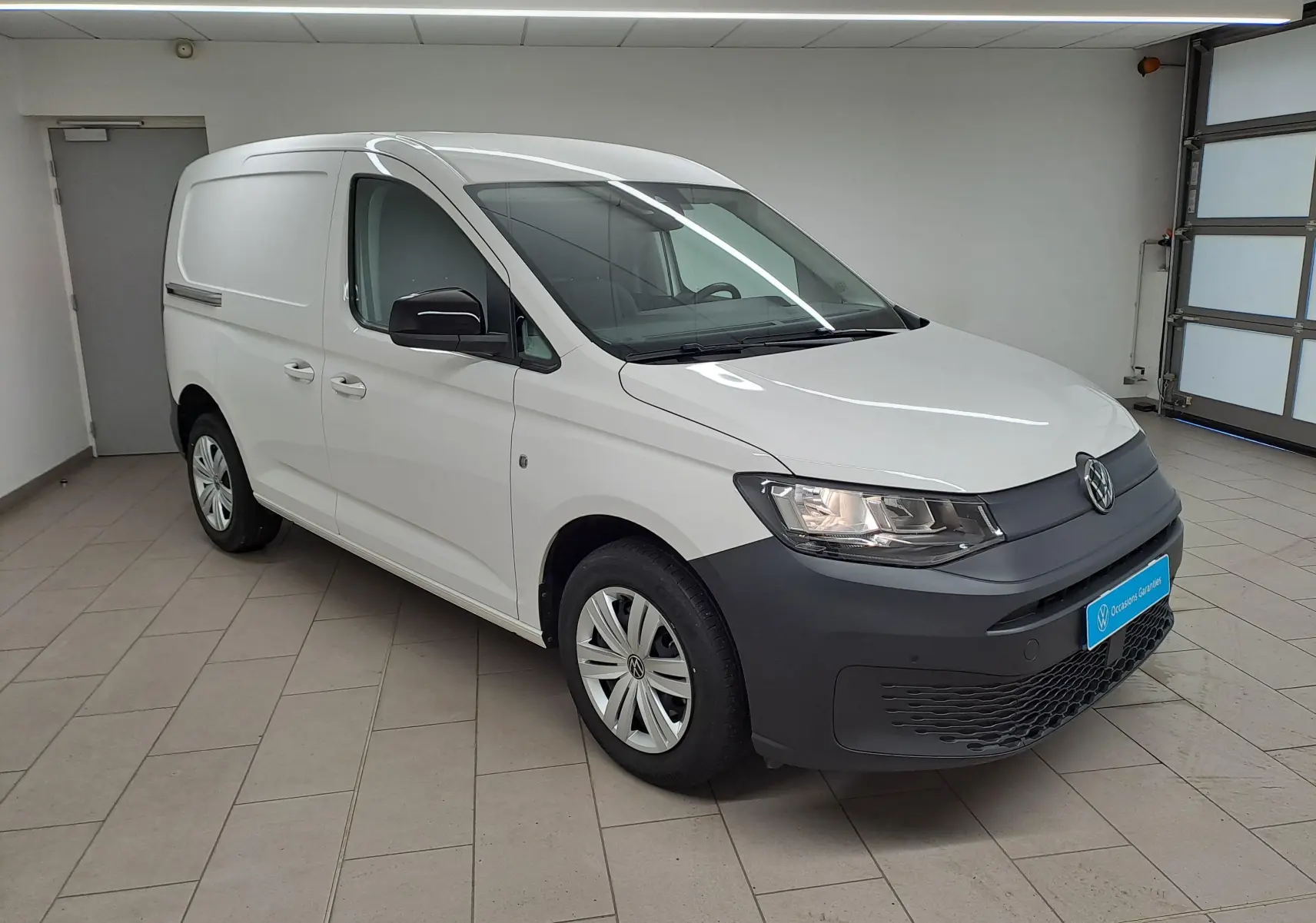 Volkswagen Caddy blanc candy en vue 3/4 avant droit, avec pare-chocs noir mat et jantes acier.