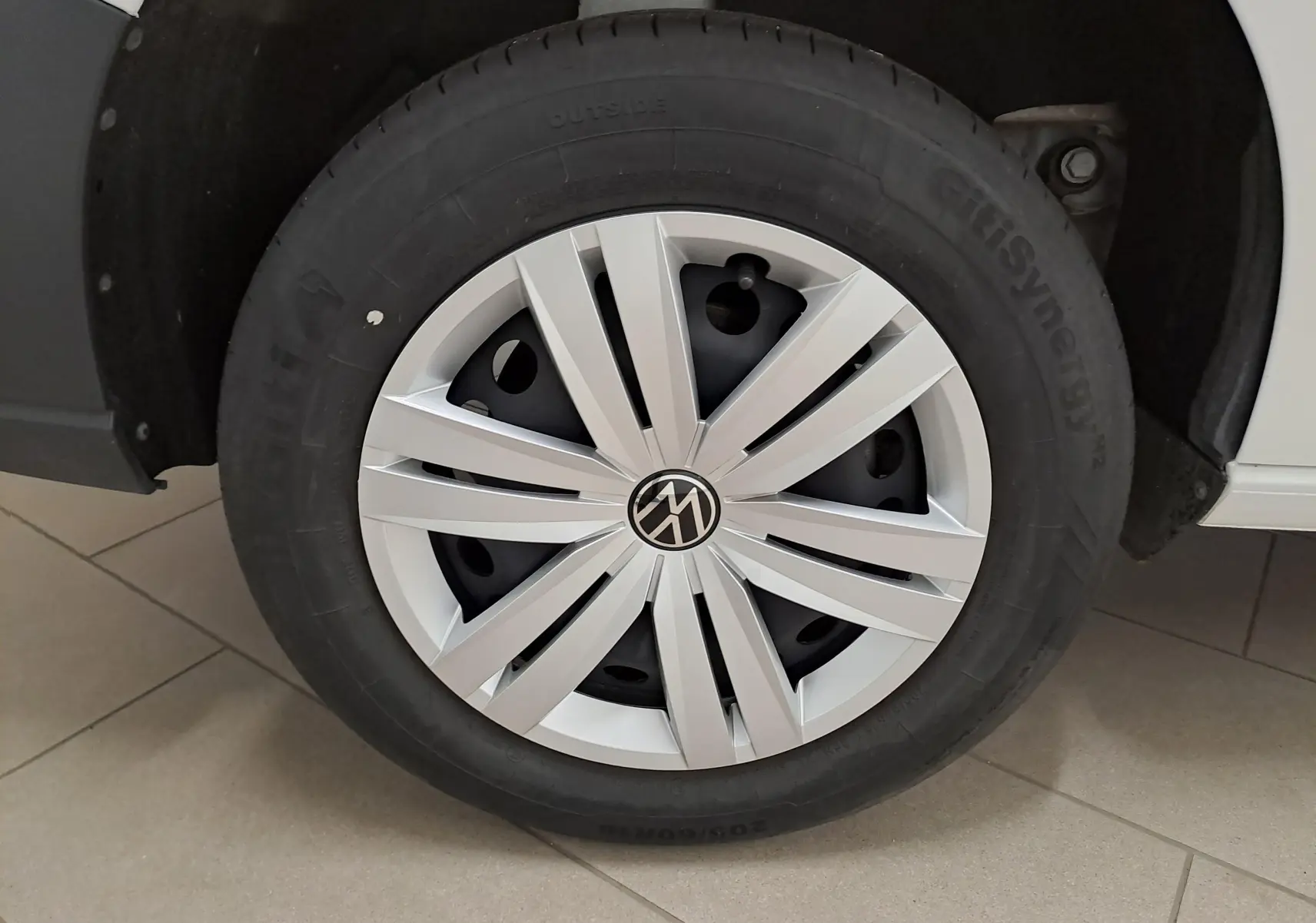 Gros plan sur la roue avant droite du Volkswagen Caddy blanc Candy avec enjoliveur argenté et logo VW central.