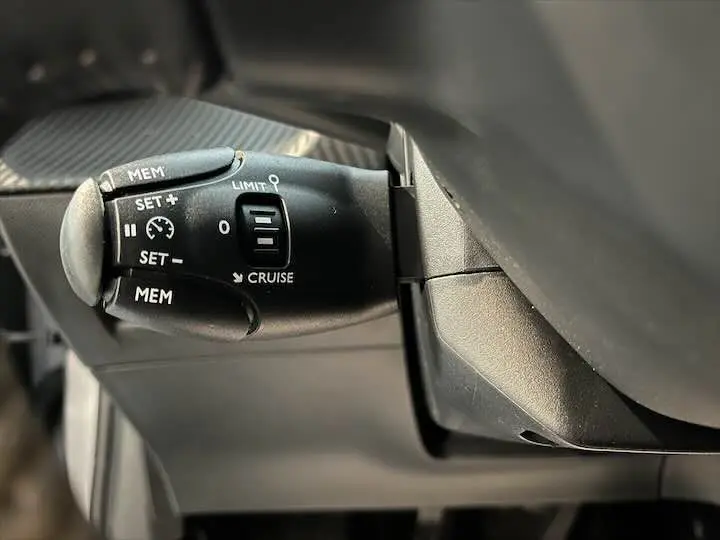 Le levier de régulateur de vitesse noir dans l'habitacle d'une Peugeot 208 1.2 100 CH S&S STYLE.