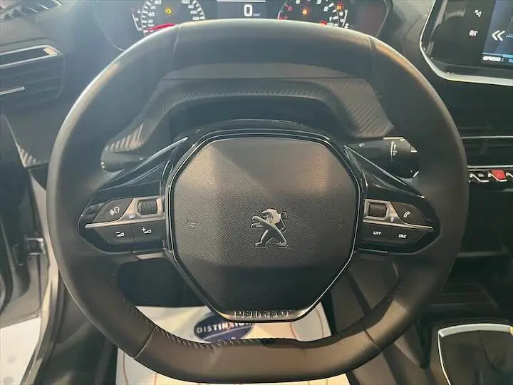 Gros plan sur le volant noir du Peugeot 208 1.2 100 CH Style, mettant en valeur les commandes intégrées et le logo lion central.
