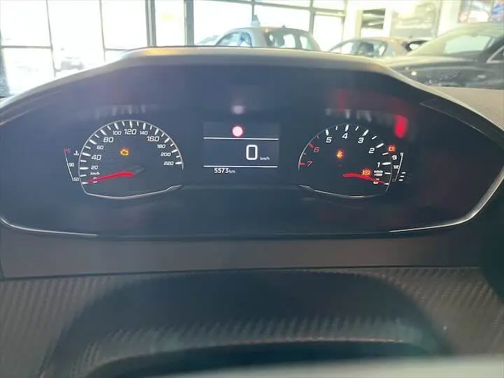Tableau de bord numérique de Peugeot 208 gris Artense, affichant 5573 km et voyants d'alerte allumés.