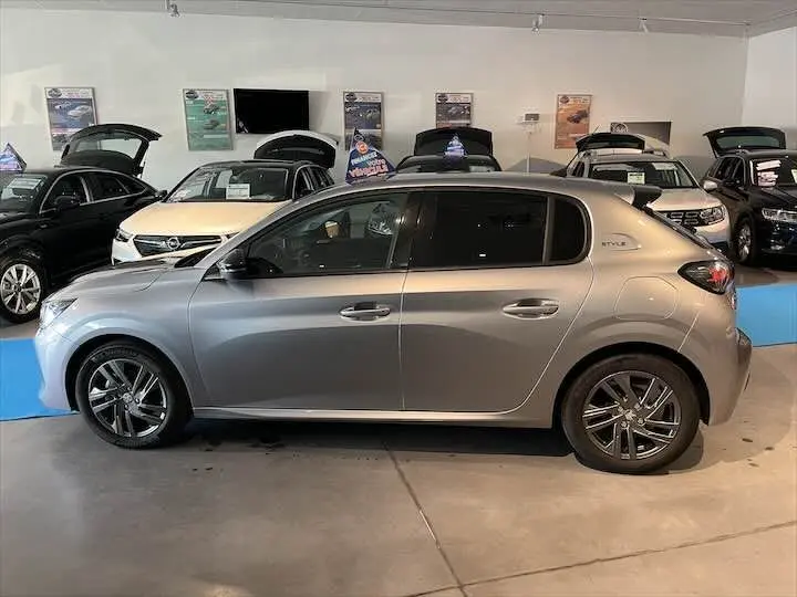 Peugeot 208 gris Artense métal vue de profil côté gauche en intérieur de showroom avec jantes alliage.
