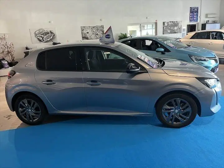 Profil côté gauche d'une Peugeot 208 gris Artense métal 2022 exposée en showroom avec jantes alliage foncé.