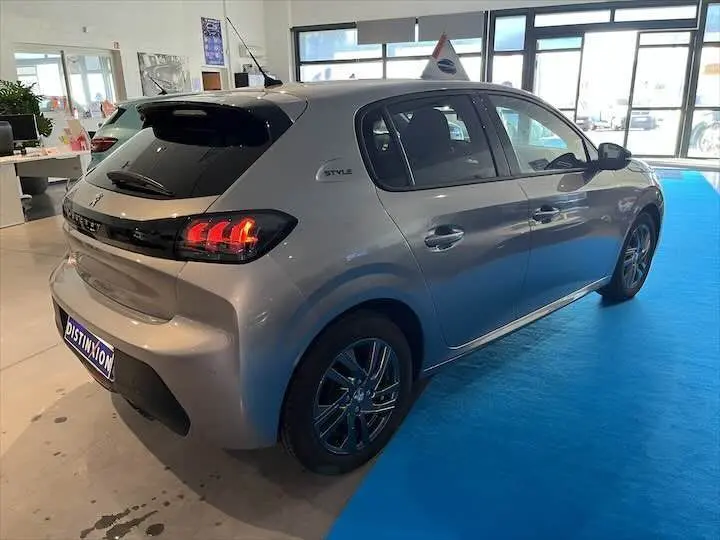 Peugeot 208 gris Artense métal vue 3/4 arrière droit en showroom avec feux arrière allumés et badge Style.