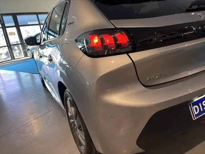 Vue 3/4 arrière droite d'une Peugeot 208 gris Artense métal avec feux arrière allumés et badge Style visible.
