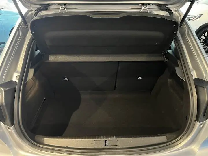 Coffre ouvert vu de l'arrière d'une Peugeot 208 gris Artense métal, montrant l'espace de chargement vide.